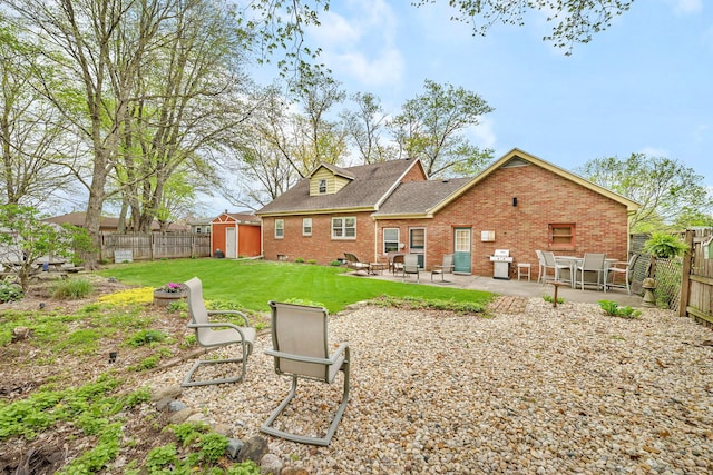 back of house featuring a yard, brick siding, a shed, a patio, and a fenced backyard
