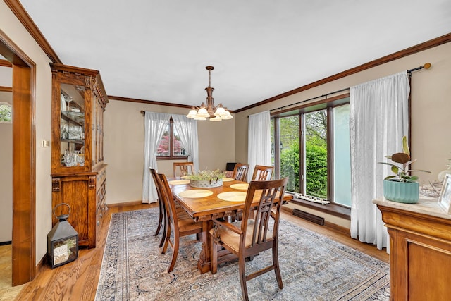 dining space featuring light wood-type flooring, a notable chandelier, crown molding, and baseboards
