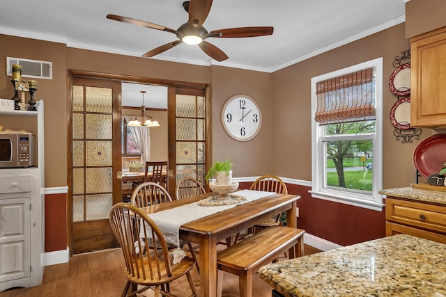 dining room with baseboards, ornamental molding, visible vents, ceiling fan with notable chandelier, and wood finished floors