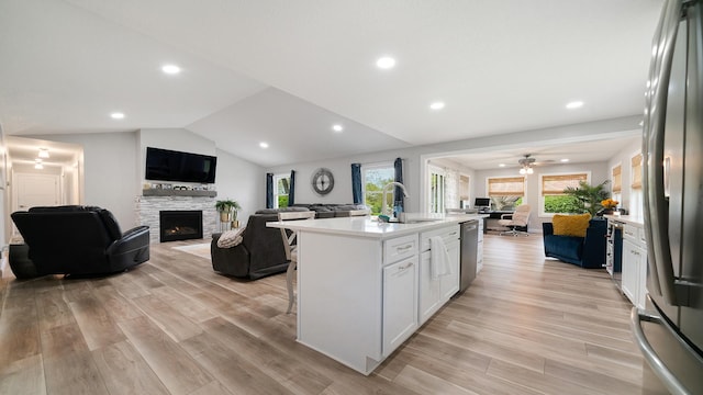 kitchen featuring stainless steel appliances, light countertops, open floor plan, white cabinets, and a stone fireplace
