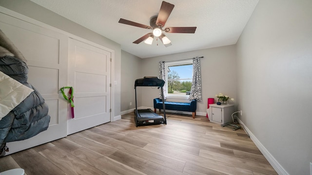 workout room with baseboards, ceiling fan, and light wood-type flooring