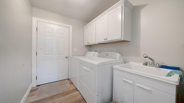 washroom with a textured ceiling, light wood finished floors, washer and dryer, a sink, and cabinet space
