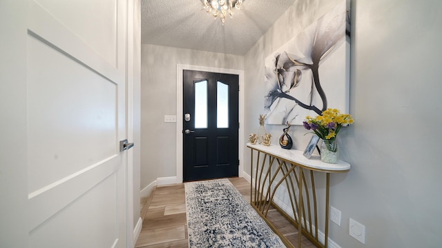 foyer with light wood finished floors, a textured ceiling, and baseboards