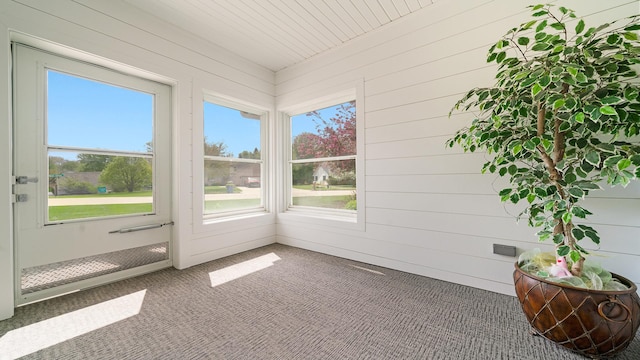 unfurnished sunroom featuring carpet flooring, a wealth of natural light, and wooden walls