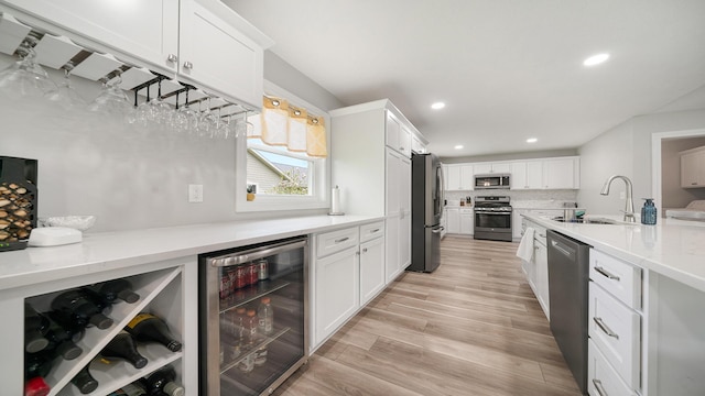 kitchen featuring a sink, stainless steel appliances, wine cooler, light wood finished floors, and white cabinets