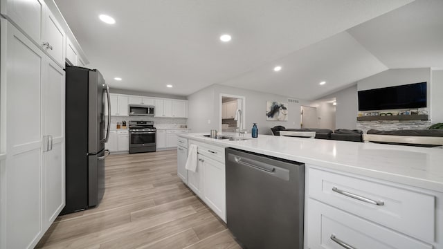 kitchen featuring light wood finished floors, a sink, open floor plan, white cabinets, and appliances with stainless steel finishes