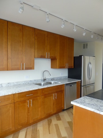 kitchen with brown cabinetry, visible vents, a sink, track lighting, and stainless steel appliances