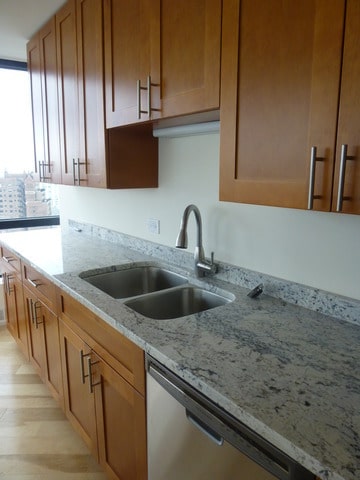 kitchen with stainless steel dishwasher, light stone counters, a sink, and light wood-type flooring