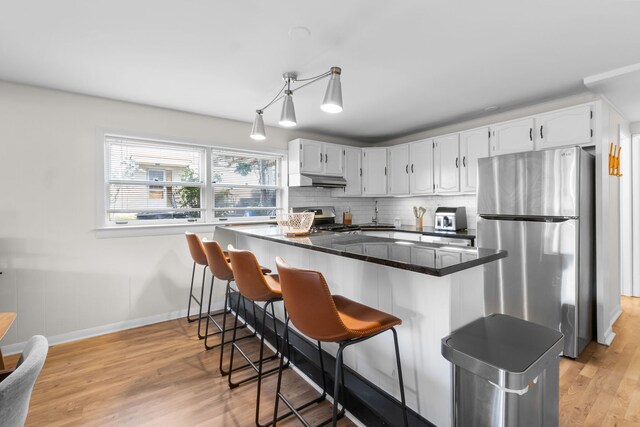 kitchen with dark countertops, light wood-style floors, stainless steel appliances, white cabinetry, and baseboards