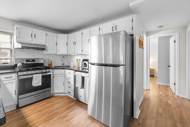 kitchen featuring appliances with stainless steel finishes, dark countertops, a sink, under cabinet range hood, and white cabinetry