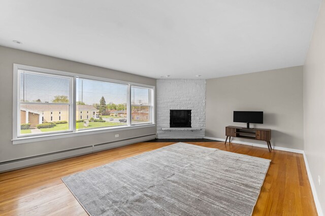 unfurnished living room featuring a large fireplace, a baseboard radiator, baseboards, and wood finished floors