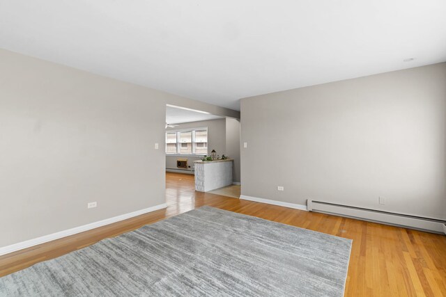 spare room with baseboards, a baseboard heating unit, and light wood-style floors