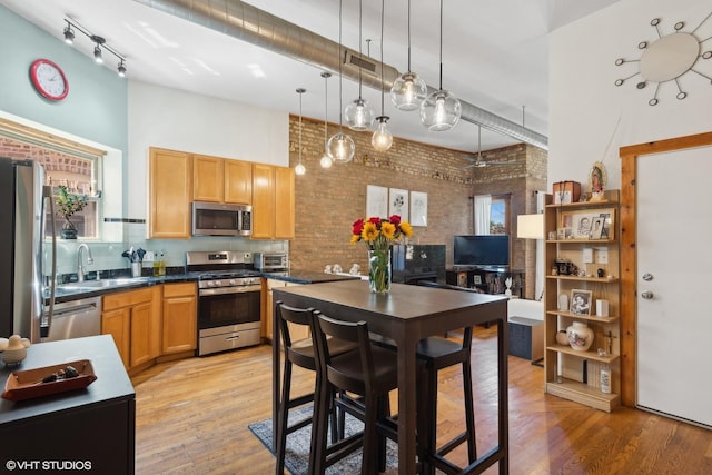 kitchen with a sink, appliances with stainless steel finishes, brick wall, dark countertops, and light wood-style floors