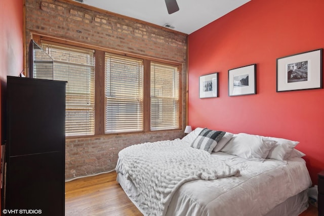 bedroom with brick wall, multiple windows, and wood finished floors
