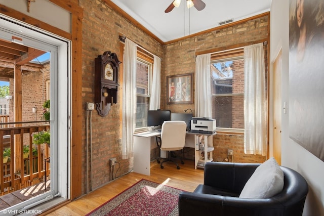 office space featuring brick wall, ceiling fan, visible vents, wood finished floors, and built in desk