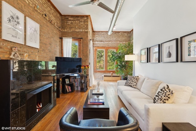 living room with wood finished floors, a towering ceiling, a fireplace, ceiling fan, and brick wall