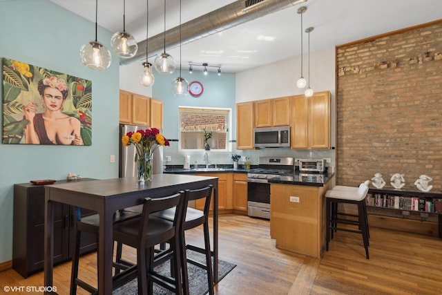 kitchen with a peninsula, stainless steel appliances, light wood-style flooring, a high ceiling, and dark countertops