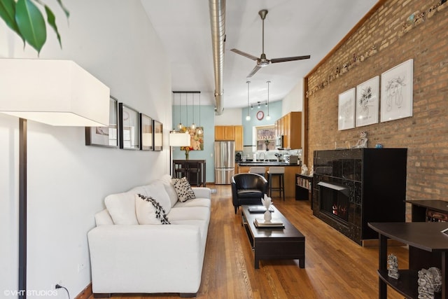 living room featuring brick wall, a tile fireplace, a ceiling fan, and wood finished floors