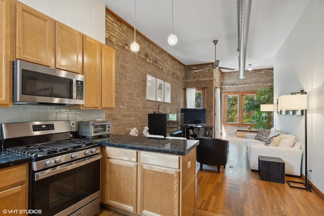 kitchen featuring brick wall, a peninsula, open floor plan, wood finished floors, and appliances with stainless steel finishes