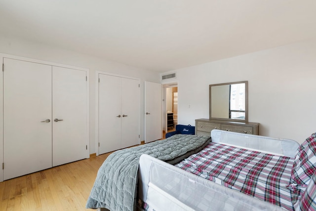 bedroom featuring visible vents, light wood-style flooring, and multiple closets