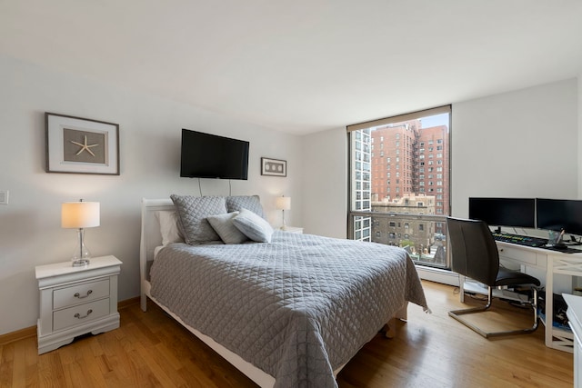 bedroom featuring baseboards, a wall of windows, and light wood-type flooring