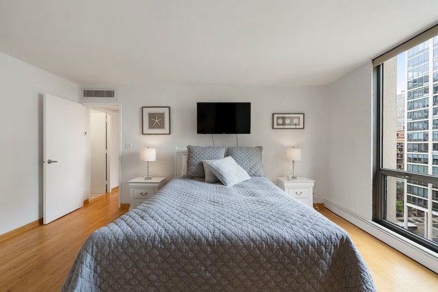 bedroom with baseboards, visible vents, baseboard heating, and light wood-type flooring
