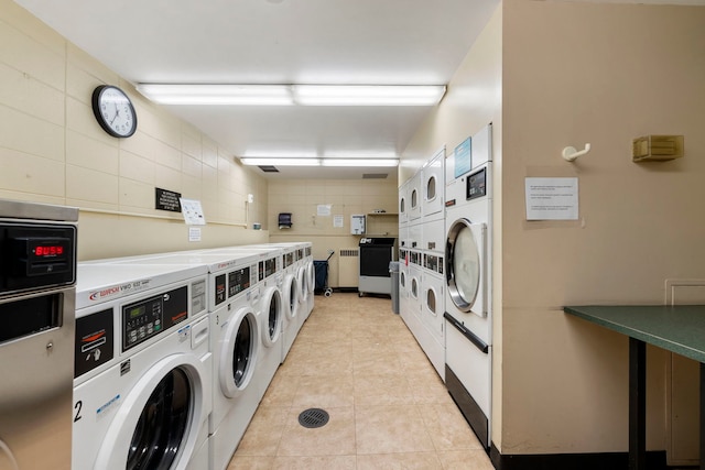 common laundry area featuring washer and dryer, light tile patterned flooring, radiator heating unit, and stacked washer and clothes dryer