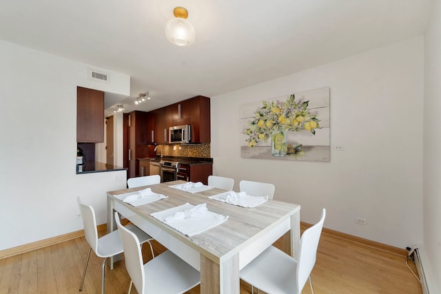dining space featuring a baseboard heating unit, baseboards, visible vents, and light wood-type flooring
