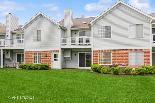 back of house featuring brick siding, a yard, central air condition unit, a chimney, and a balcony
