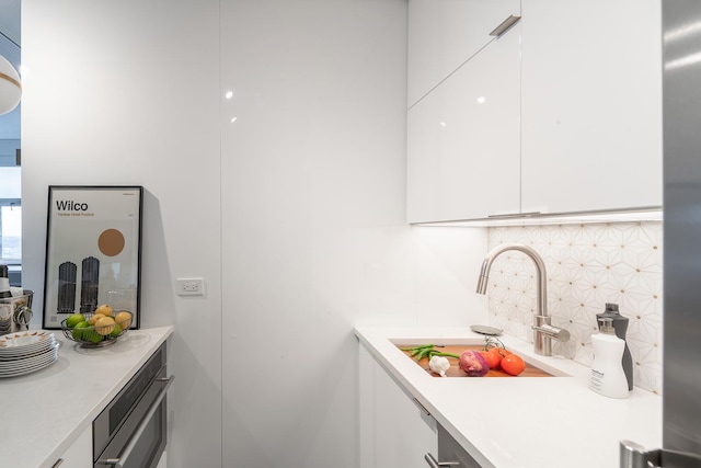 kitchen featuring white cabinets, decorative backsplash, modern cabinets, light countertops, and a sink