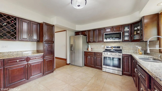 kitchen featuring light stone countertops, glass insert cabinets, a sink, appliances with stainless steel finishes, and backsplash
