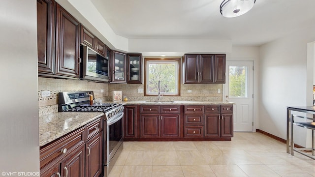 kitchen featuring a healthy amount of sunlight, decorative backsplash, appliances with stainless steel finishes, a sink, and light stone counters