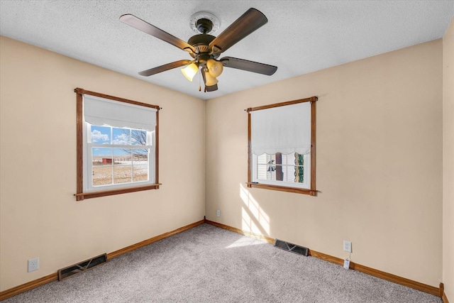 carpeted spare room featuring a textured ceiling, baseboards, visible vents, and ceiling fan