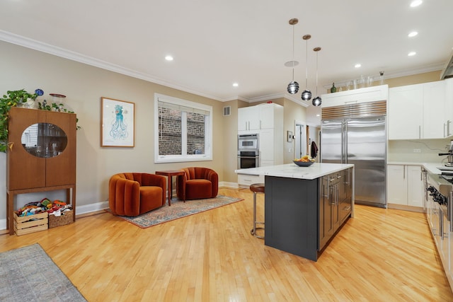 kitchen featuring stainless steel appliances, ornamental molding, white cabinets, a kitchen island, and light wood-style flooring