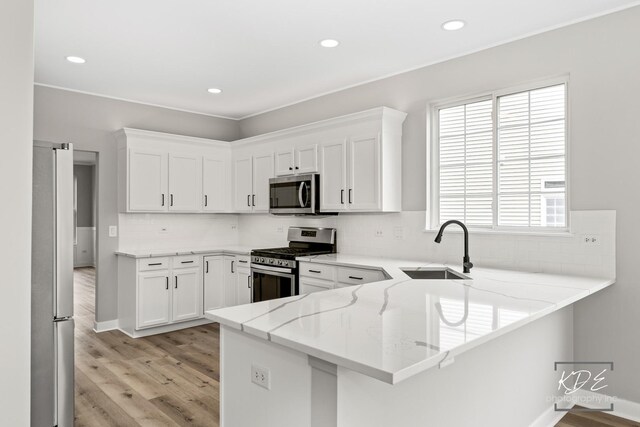 kitchen with appliances with stainless steel finishes, light stone countertops, a sink, a peninsula, and light wood-style floors
