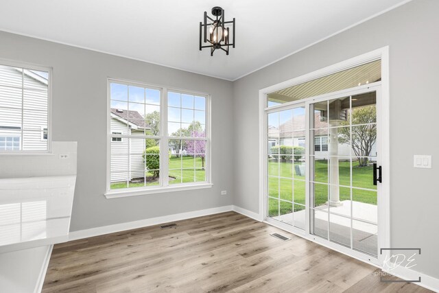 unfurnished dining area with baseboards, a notable chandelier, wood finished floors, and visible vents