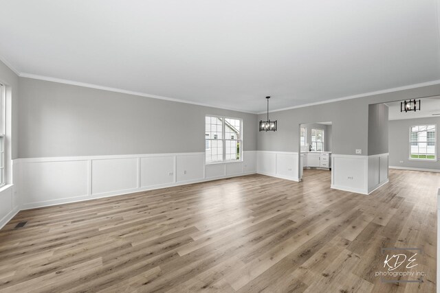 interior space with crown molding, a wainscoted wall, light wood-style floors, and a notable chandelier