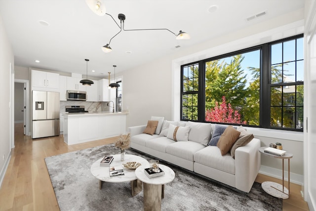 living room featuring light wood-style floors, baseboards, recessed lighting, and visible vents