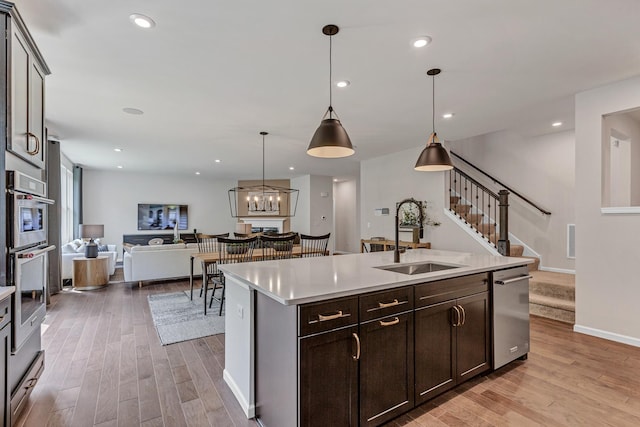 kitchen featuring a sink, light wood finished floors, dishwasher, light countertops, and open floor plan