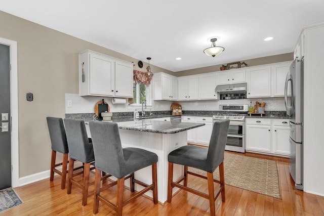 kitchen featuring decorative backsplash, a kitchen bar, under cabinet range hood, white cabinets, and stainless steel appliances