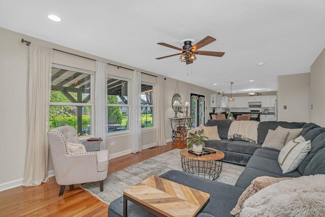 living area with baseboards, a ceiling fan, and light wood-style flooring