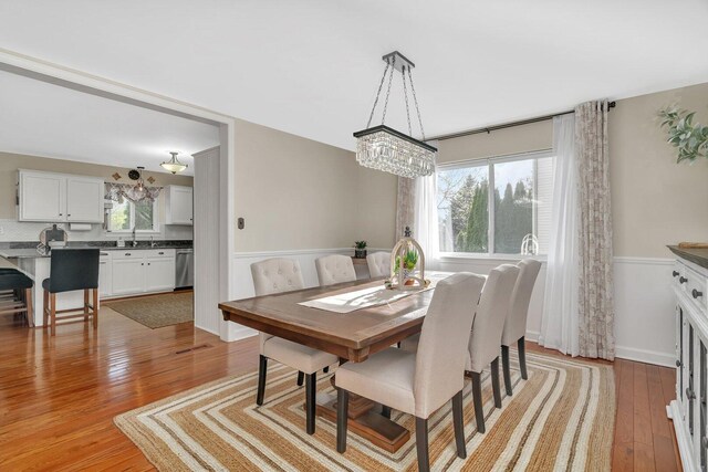 dining space with a notable chandelier, plenty of natural light, light wood-style flooring, and a wainscoted wall