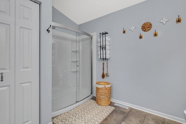 bathroom with baseboards, visible vents, a shower stall, and vaulted ceiling