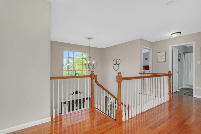 hall with a notable chandelier, an upstairs landing, baseboards, and hardwood / wood-style flooring