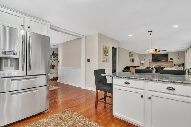 kitchen featuring a fireplace, open floor plan, stainless steel fridge, white cabinets, and light wood finished floors