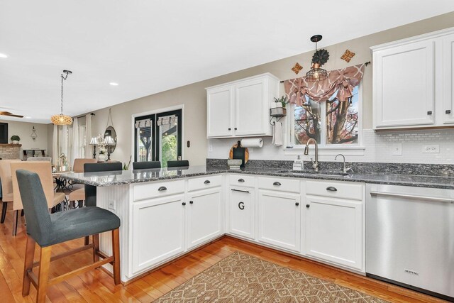 kitchen with stainless steel dishwasher, a sink, white cabinets, a peninsula, and light wood-style flooring