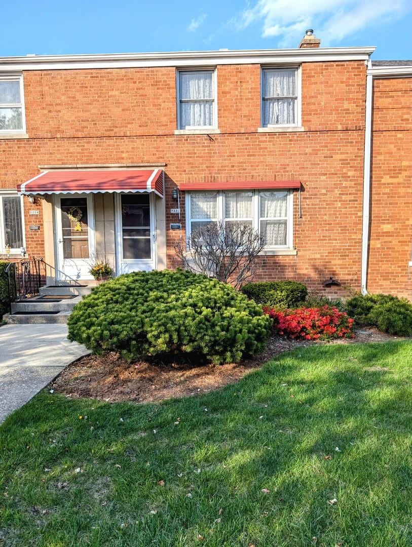 view of property with a front lawn, brick siding, and a chimney