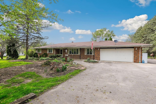 single story home featuring a chimney, driveway, brick siding, and an attached garage