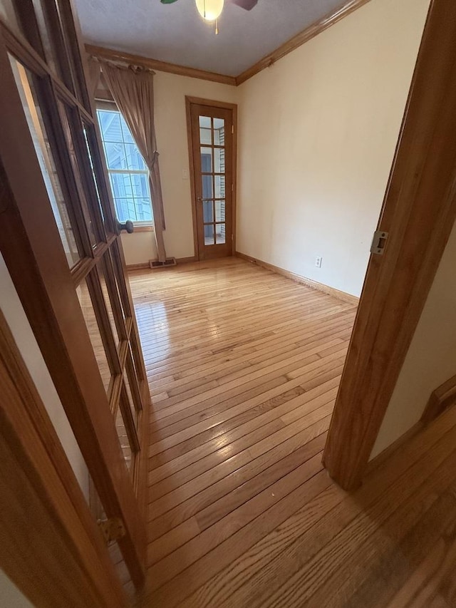 spare room featuring light wood-style floors, baseboards, ornamental molding, and a ceiling fan
