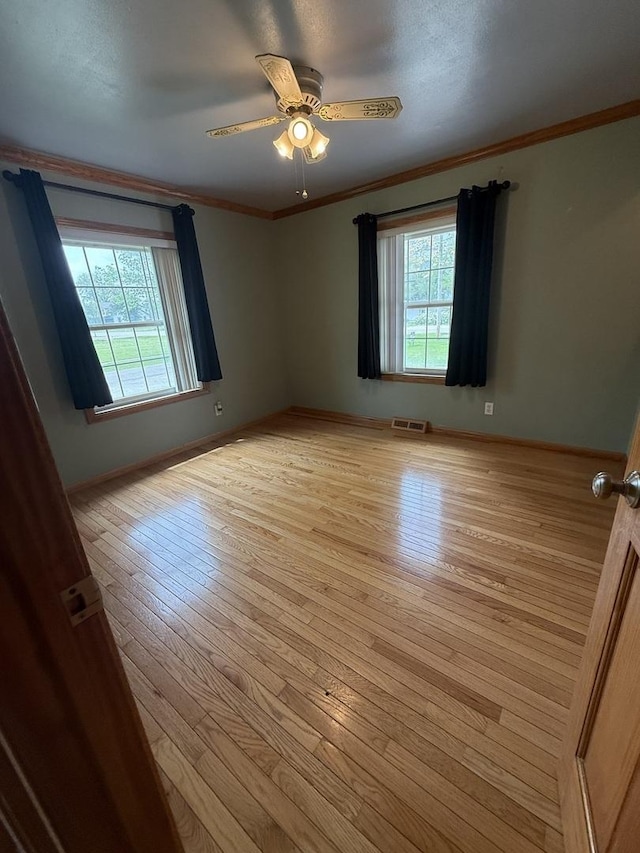empty room featuring a ceiling fan, visible vents, crown molding, baseboards, and light wood finished floors
